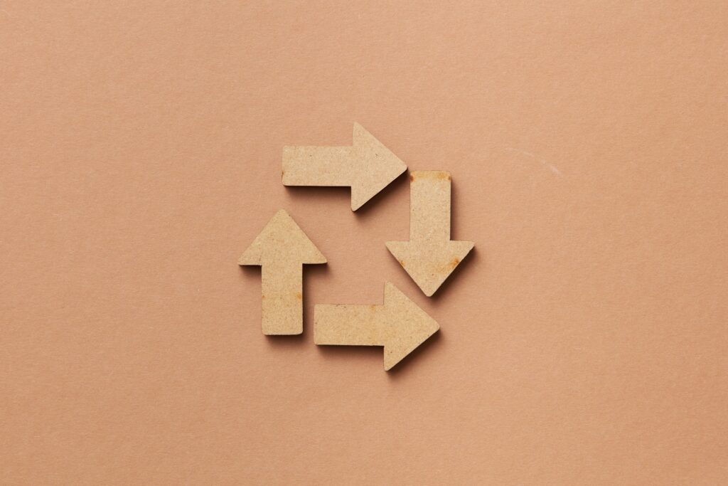 Close-up of a recycling symbol made from wooden arrows on a beige background.